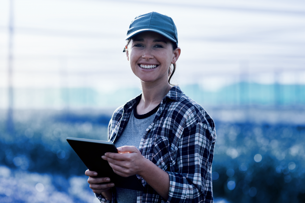 A female farmer standing in a field, holding a tablet in her hands.
