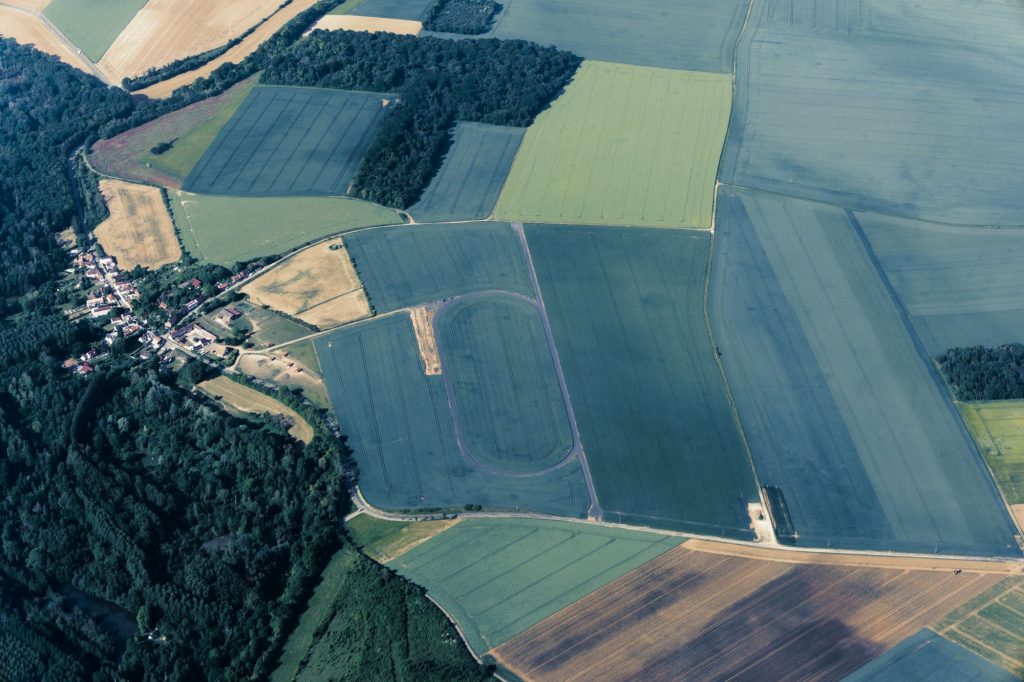 Aerial view of patchwork farmland with fields in various shades and a small village near a forested area